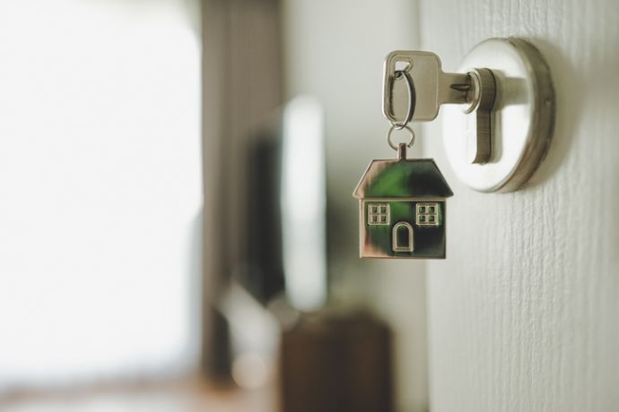 Een sleutel met sleutelhanger in de vorm van een huis zit op de deur