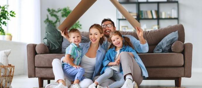 Gelukkig gezin zit op de grond voor de zetel, in hun vochtvrije woning met kartonnen dak boven hun hoofd